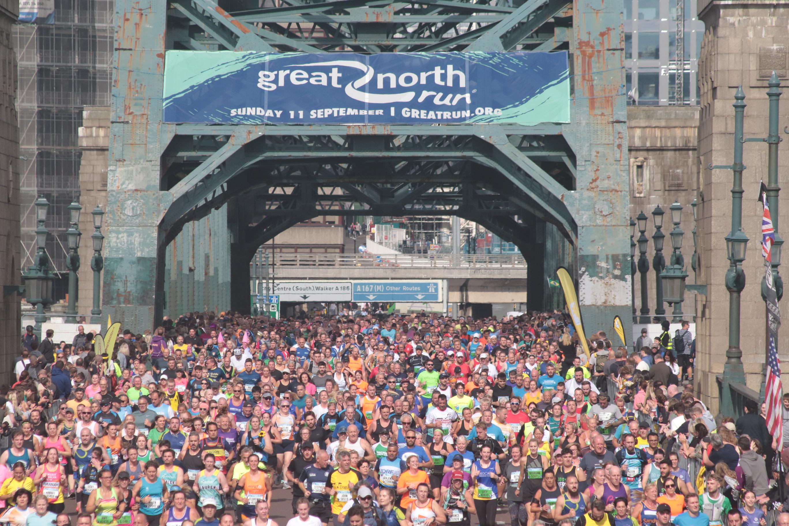 Photo of runners crossing the tyne bridge during the Great North Run. I am in the crowd wearing a red running shirt and a white cap.