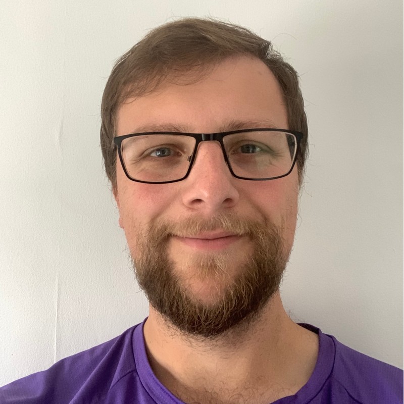 Photo of me! I am a white man with brown hair, a beard and glasses, and I'm pictured wearing a purple T shirt